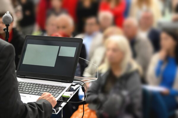 Close up of businessman typing on laptop, additionally blurred audience in background