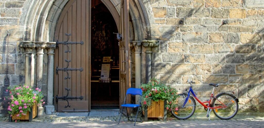 Open wooden door of church in Northern Germany. Blue folding chair at entry and bicycle at wall.