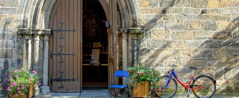 Open wooden door of church in Northern Germany. Blue folding chair at entry and bicycle at wall.