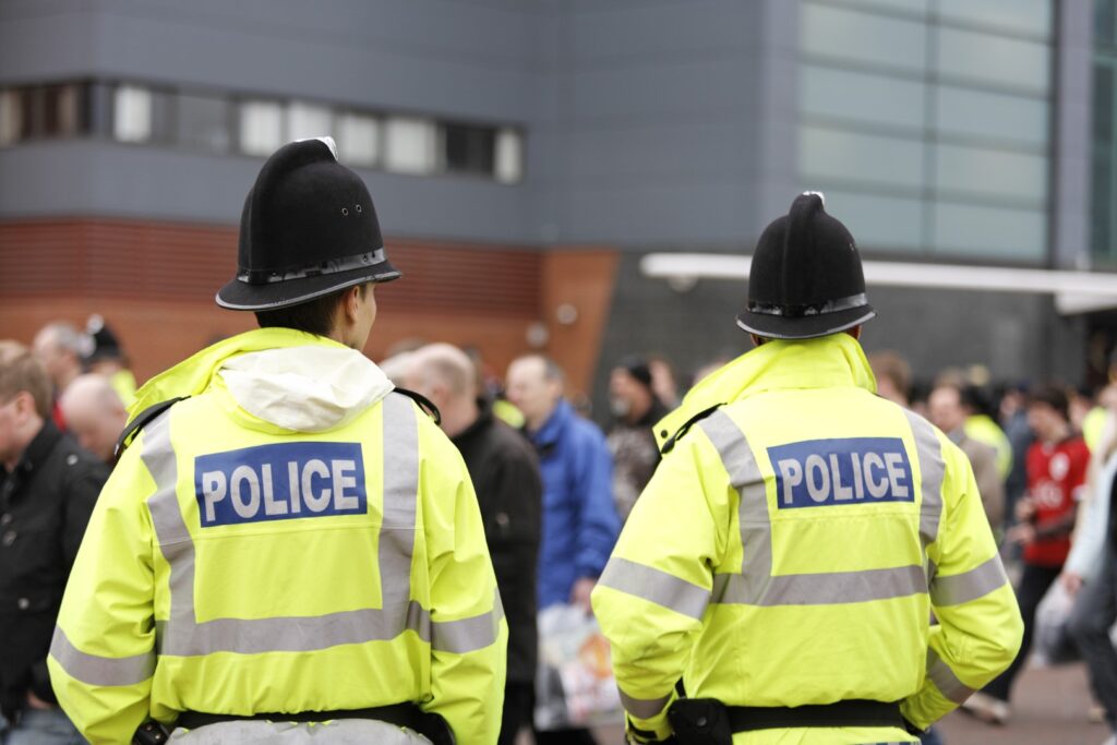 Two British Policemen-Traditional Helmets-Crowd Control. More below...