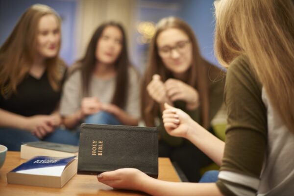 a group of four teenage girls sit at home and discuss the bibles that they are reading .