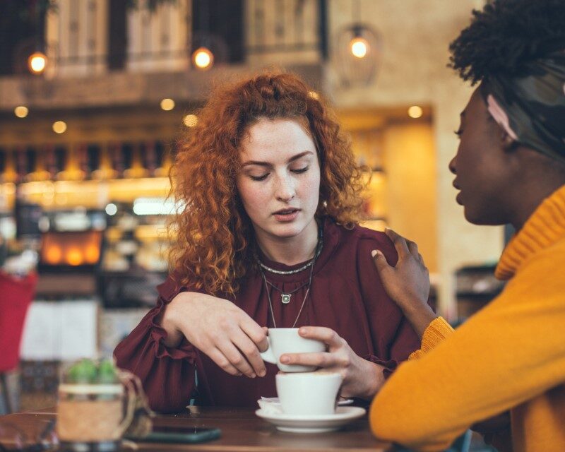 A young woman is talking with a female friend about her problem in a cafe. The friend is supportive and understanding.
