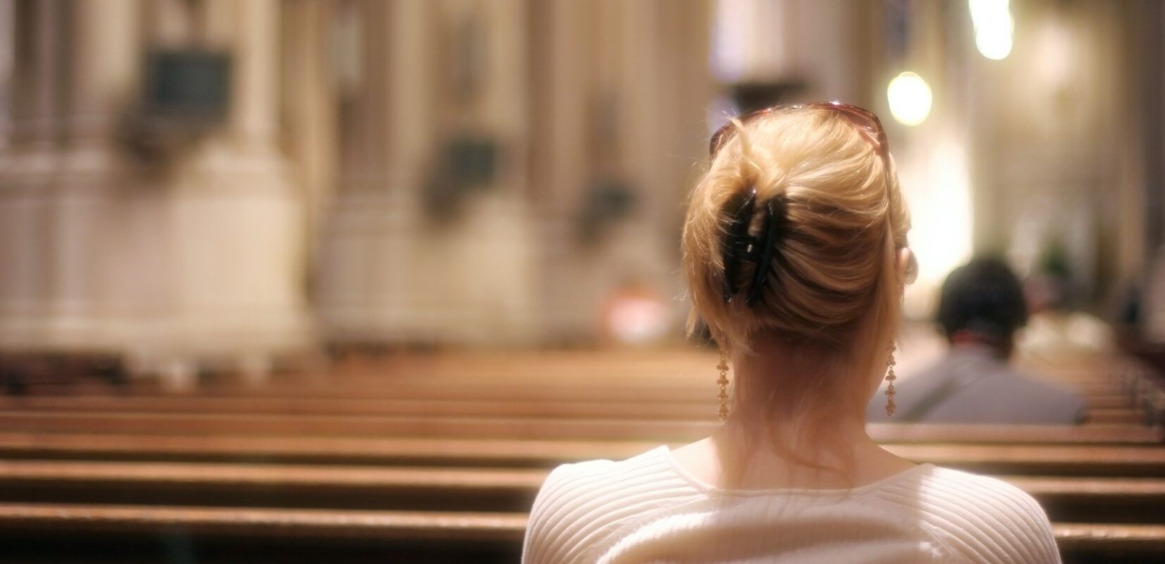 Blonde woman sitting on a church bench praying