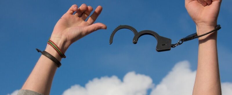 A close-up of hands with handcuffs unclipped on one hand and loose in the air