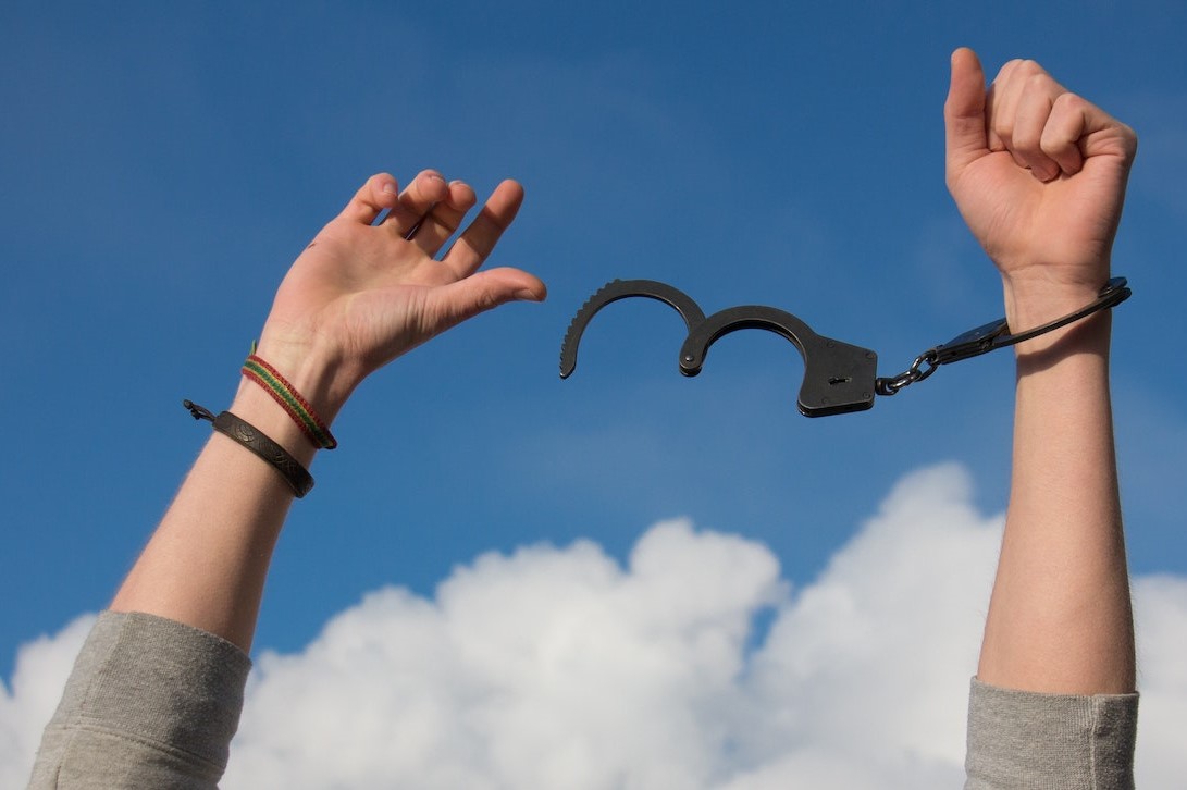 A close-up of hands with handcuffs unclipped on one hand and loose in the air