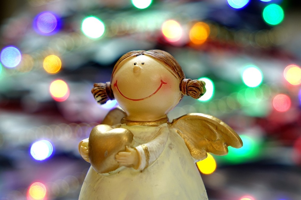 Angel figurine holding a gold heart with blurred colourful fairy lights in the background