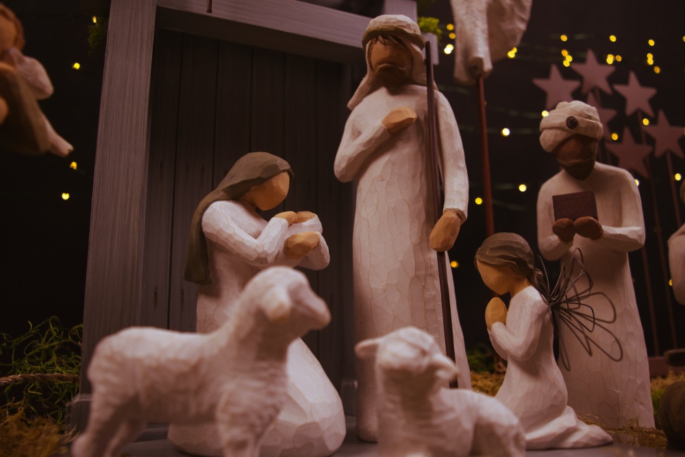 Figurines depicting the nativity. There is a sheep in the foreground and Mary holding Jesus, Joseph and a king and angel in the background of the image.