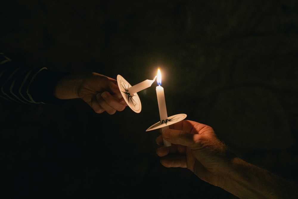 two candles one being lit from the other in the dark