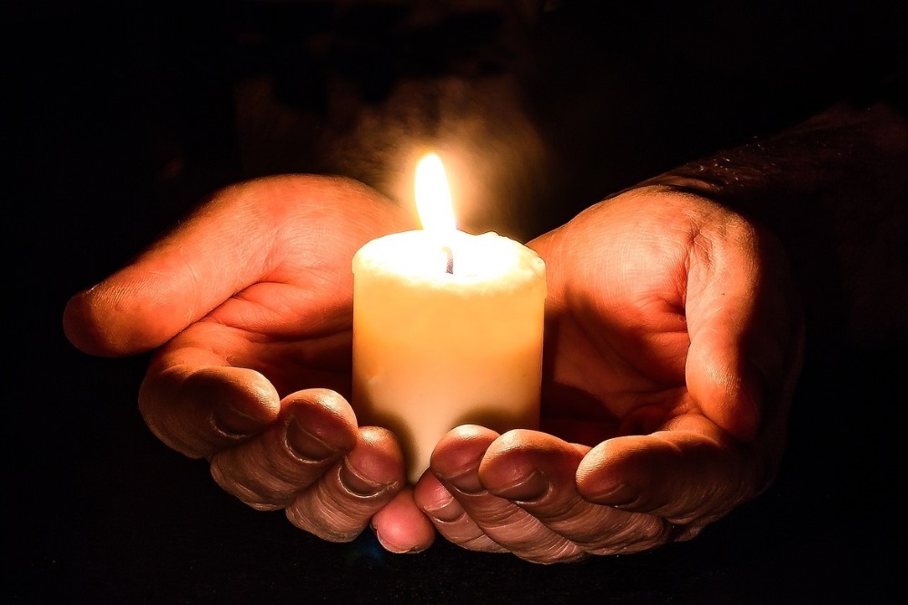 Hands holding a lit candle in darkness