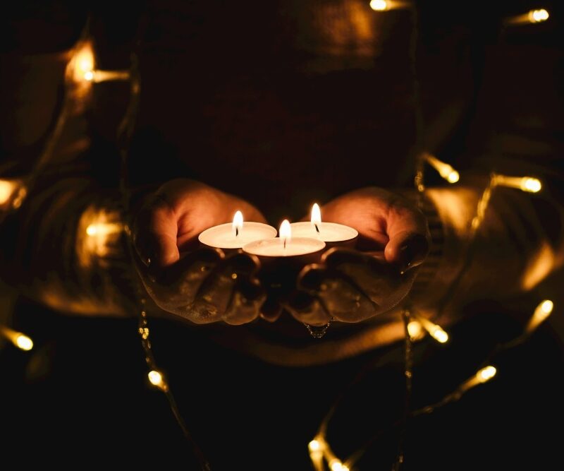 hands in the darkness holding tea lights with fairy lights wrapped around their arms