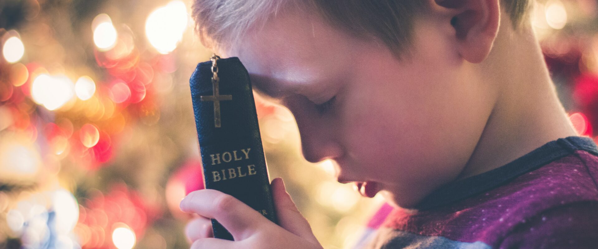 Child holding a bible and holding head down to pray