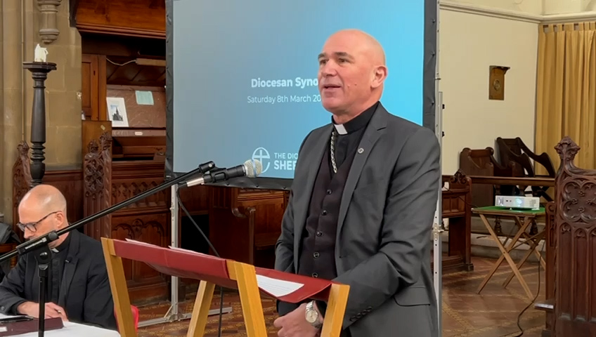 Bishop Pete stands at a podium delviering an address